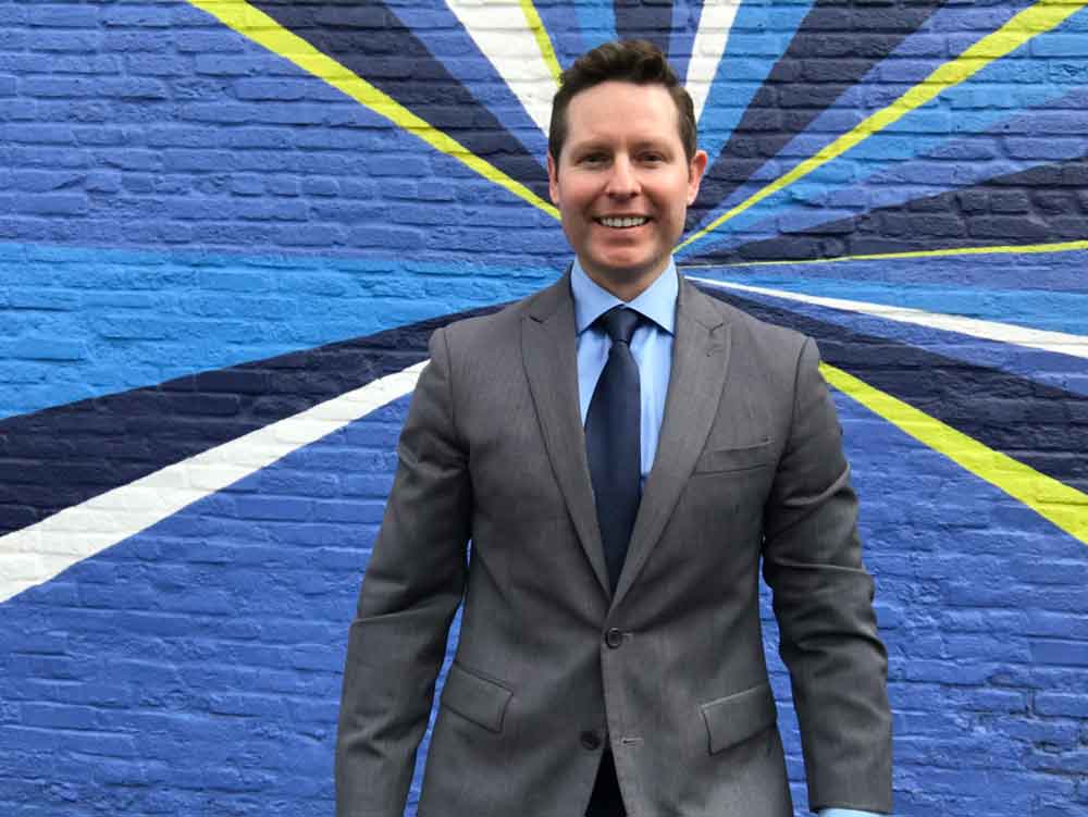 A photo of Andy DiOrio against a colorful, painted brick wall.